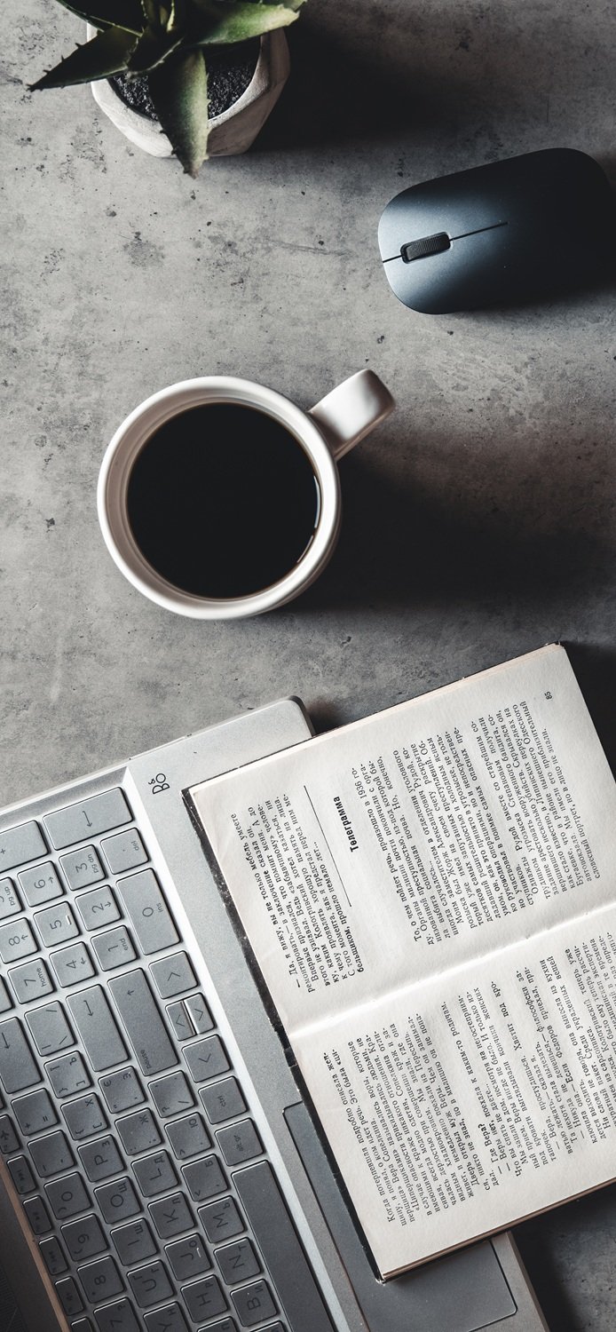 The office desk flat lay view with laptop, mouse, tree, paper clip, coffee cup, notebook, pencil, black glasses on white background.