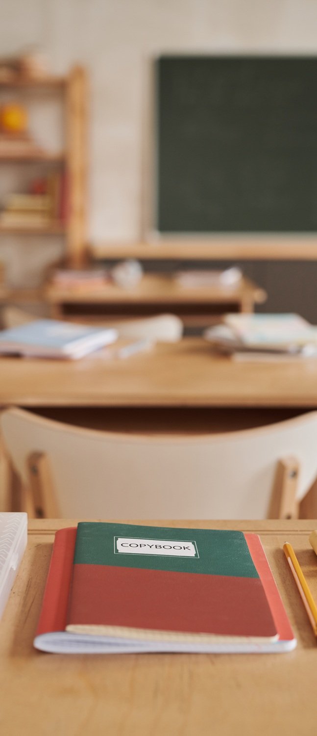 Vertical image of wooden school desks in row facing blackboard in empty classroom, focus on foreground